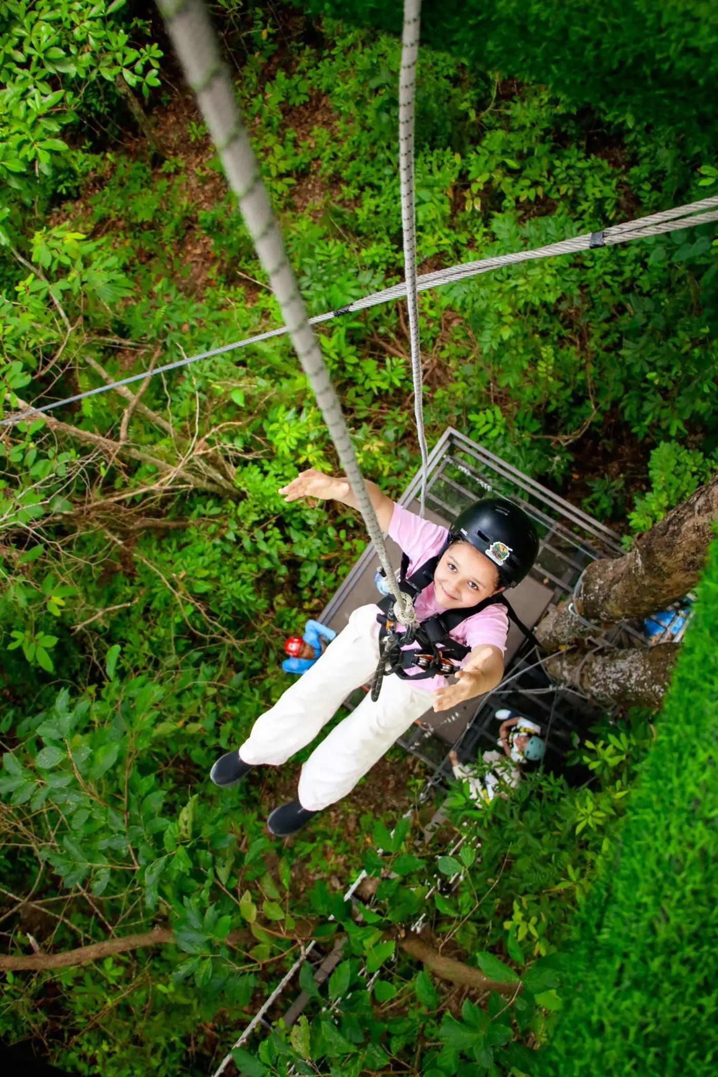 A girl glides on a zipline with arms outstretched